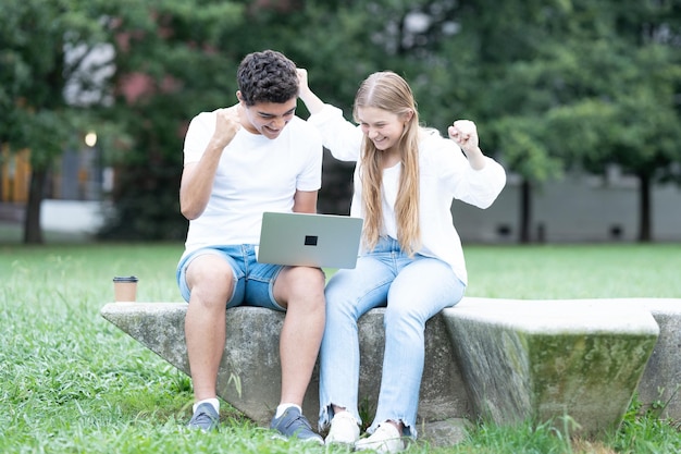 Pareja de estudiantes celebrando buenos resultados en la computadora portátil