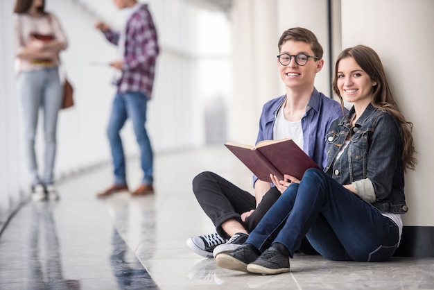 Foto pareja estudiantes sentados y leyendo un libro.