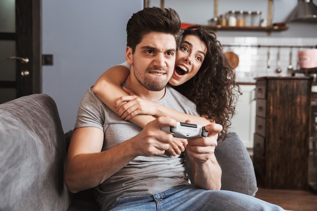 Pareja europea hombre y mujer de 30 años sentados en el sofá en casa y jugando videojuegos junto con joysticks