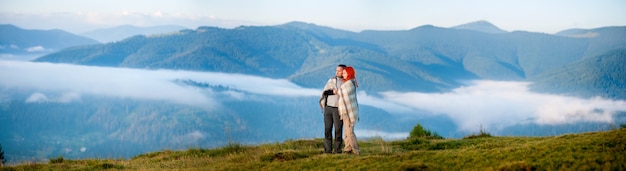 Pareja de excursionistas cubiertos con una manta de pie juntos en una colina