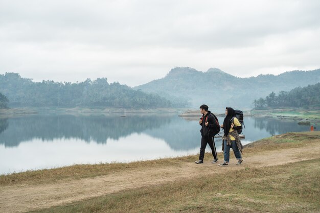 Pareja de excursionistas con mochilas caminando al lado del lago