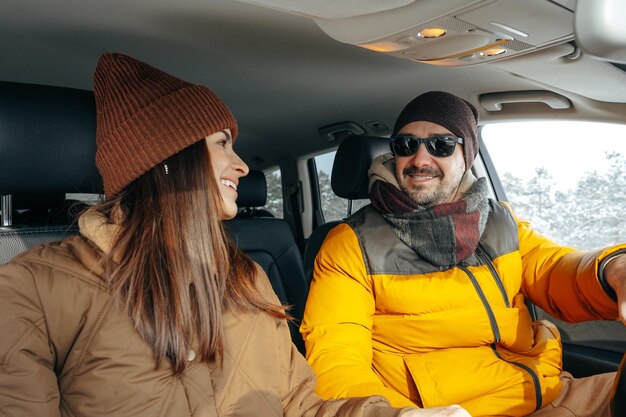 Pareja familiar sentada en un auto con ropa de invierno en un bosque nevado