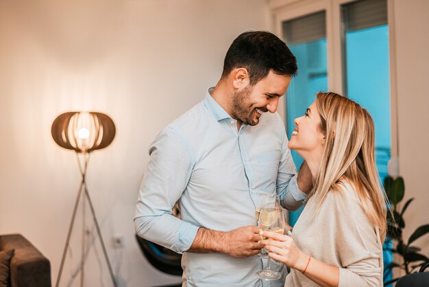 Pareja feliz abrazando mientras disfruta de vino blanco en casa.