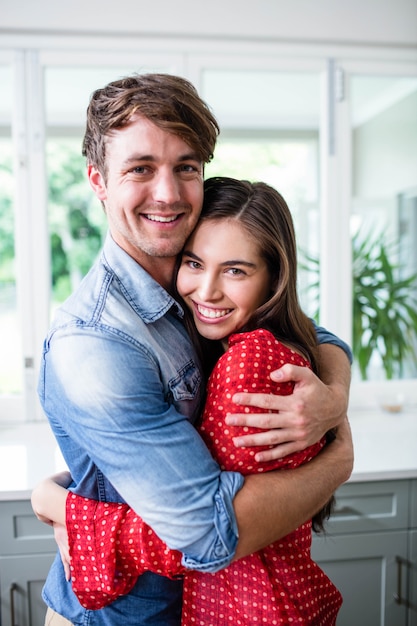 Foto pareja feliz abrazando y mirando a cámara en la cocina