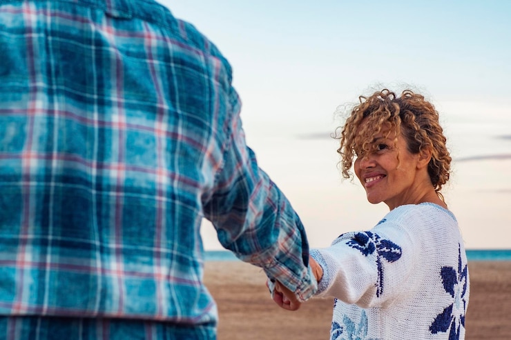 Foto pareja feliz adulta enamorada tomados de la mano y caminando juntos en la playa disfrutando de vacaciones de invierno actividad de ocio al aire libre con hombre y mujer sonriendo océano y cielo en segundo plano