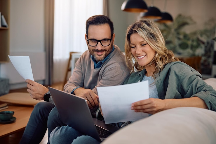 Foto una pareja feliz analizando el papeleo mientras usa una computadora portátil en casa