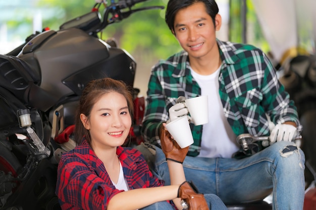 Pareja feliz bebiendo café en un taller de reparación de motocicletas