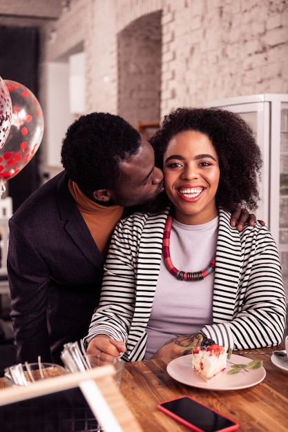 Pareja feliz. Buen hombre alegre de pie cerca de su novia mientras la besa