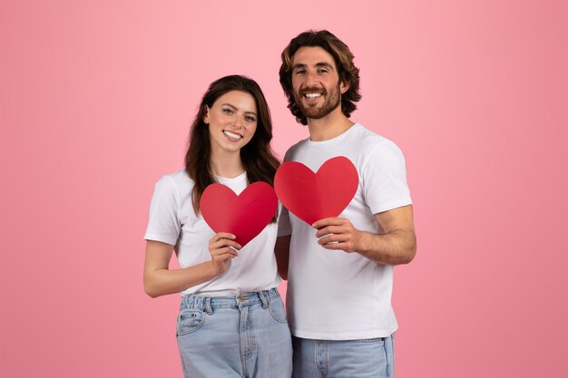 Foto una pareja feliz con camisetas blancas y vaqueros con recortes de papel en forma de corazón rojo