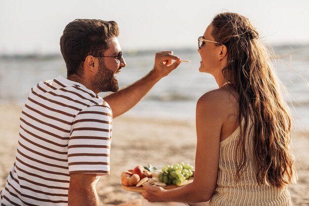 pareja feliz con comida haciendo picnic en la playa