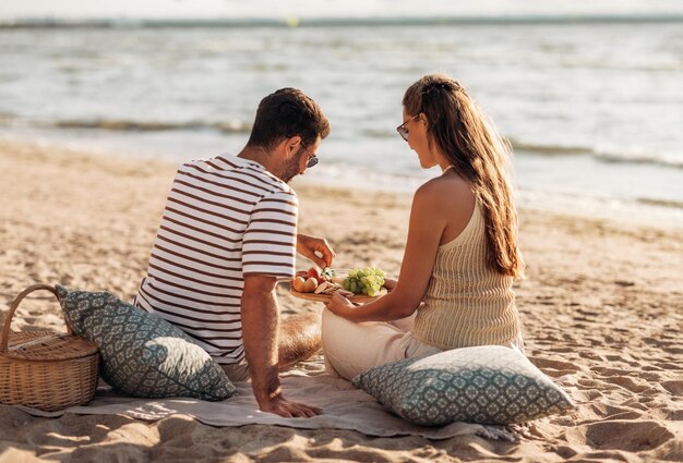 pareja feliz con comida haciendo picnic en la playa