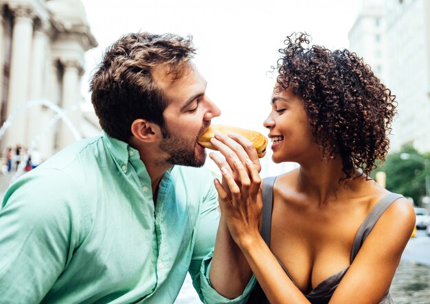 Pareja feliz comiendo hot dogs y divirtiéndose en la ciudad de Nueva York