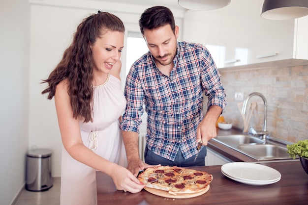 Pareja feliz comiendo pizza en su cocina