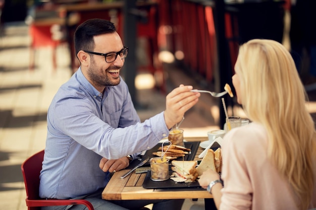 Pareja feliz comiendo en un restaurante Hombre compartiendo su comida y alimentando a su novia