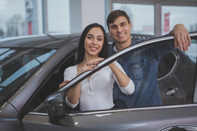 Foto pareja feliz comprando un auto nuevo en el salón del concesionario