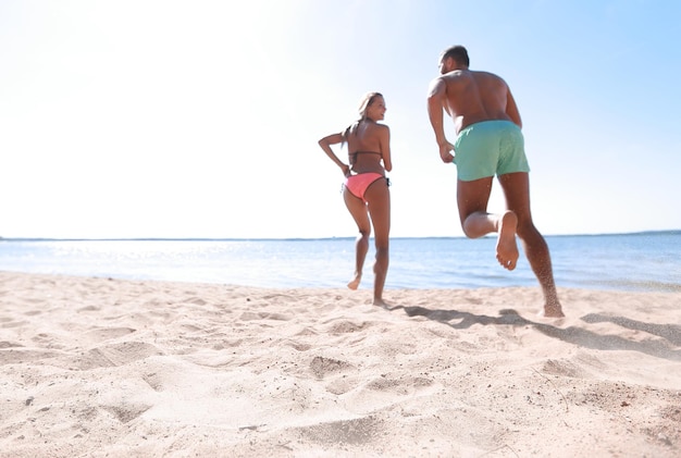 Pareja feliz corriendo en la playa tropical en vacaciones al atardecer