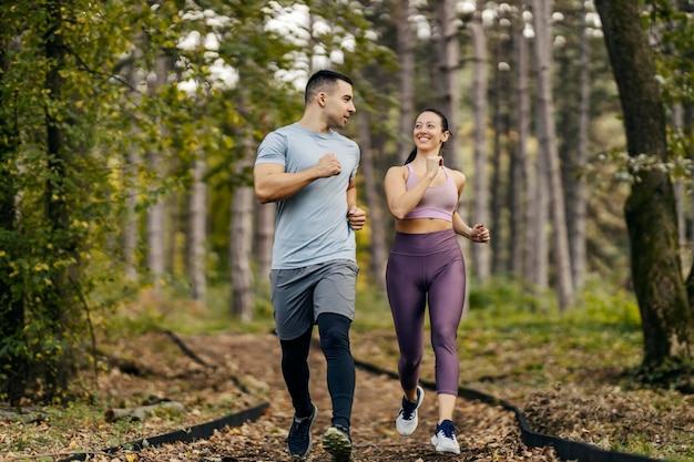 Una pareja feliz y deportiva está corriendo en el bosque.