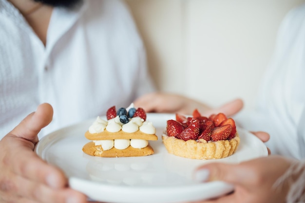 Pareja feliz desayunando en la cama con deliciosas galletas con fresas encima