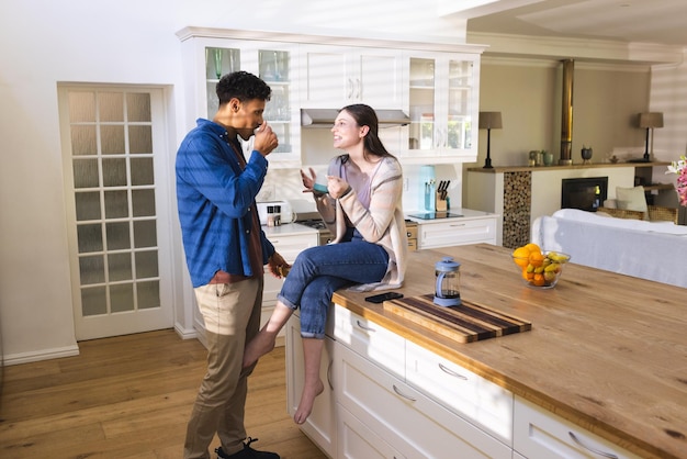 Una pareja feliz y diversa discutiendo y bebiendo té en una cocina brillante en el espacio de copia de casa