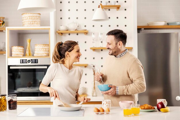 Una pareja feliz está preparando huevos para el desayuno en la mañana en casa.