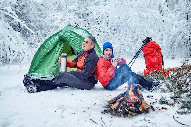 Pareja feliz en una fogata en el bosque nevado de invierno