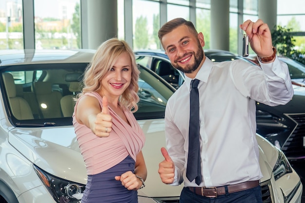 Una pareja feliz se para frente a un auto nuevo. El hombre cubrió los ojos de su esposa en la sala de exposición.