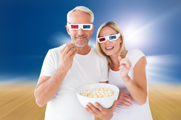 Una pareja feliz con gafas 3d comiendo palomitas contra un paisaje marrón soleado