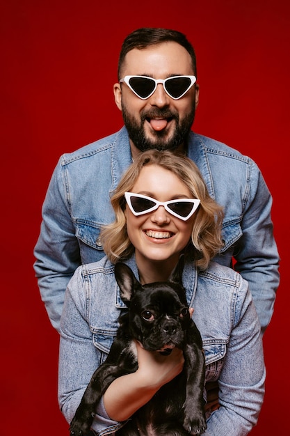 Pareja feliz con gafas de sol sosteniendo un concepto de familia feliz de bulldog francés