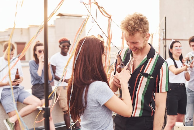 Foto pareja feliz grupo de jóvenes con ropa informal tienen una fiesta en la azotea juntos durante el día