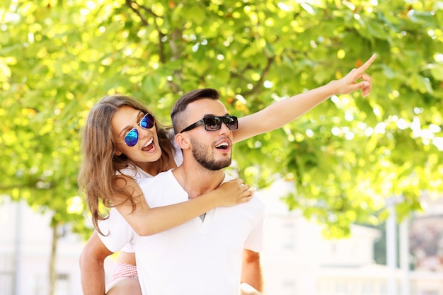 Una pareja feliz haciendo caballito y apuntando a algo en el parque.