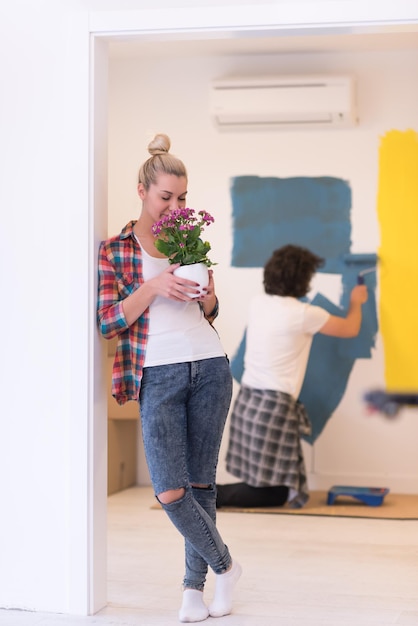 Pareja feliz haciendo renovaciones en el hogar, el hombre está pintando la habitación y la mujer sostiene la olla con flores