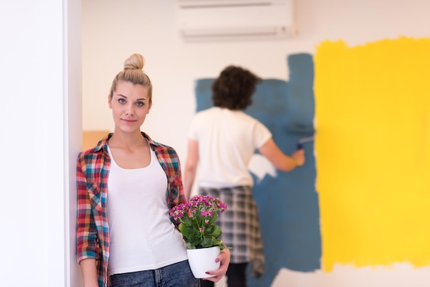 Pareja feliz haciendo renovaciones en el hogar, el hombre está pintando la habitación y la mujer sostiene la olla con flores