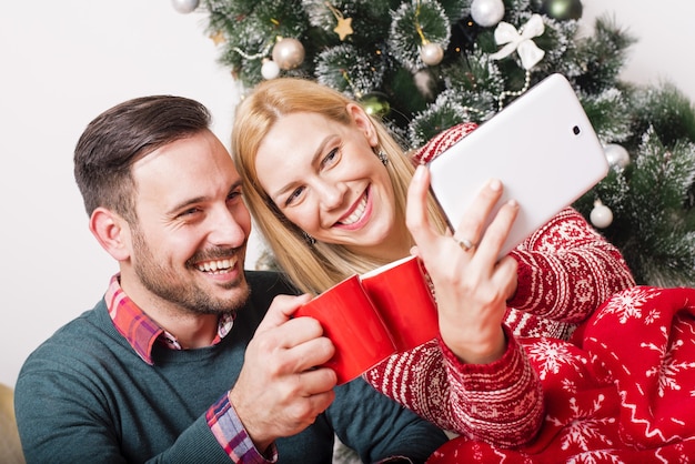 Pareja feliz haciendo un selfie sobre un fondo de árbol de navidad