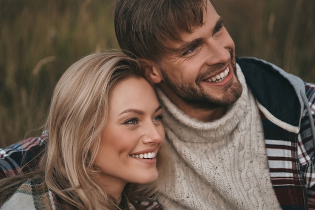 Pareja feliz. Hermosa joven pareja abrazándose y mirando a otro lado con una sonrisa mientras está sentado en el campo