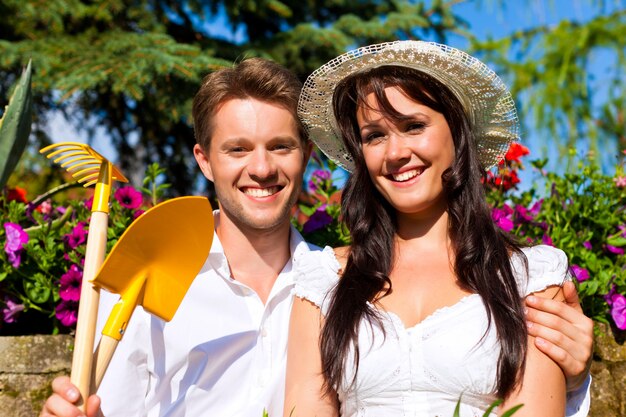 Pareja feliz con herramientas de jardinería en jardín de flores iluminado por el sol