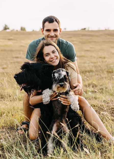 Una pareja feliz de hombre y mujer al aire libre abrazando a un schnauzer gigante negro y a un perro Schnauzer en miniatura