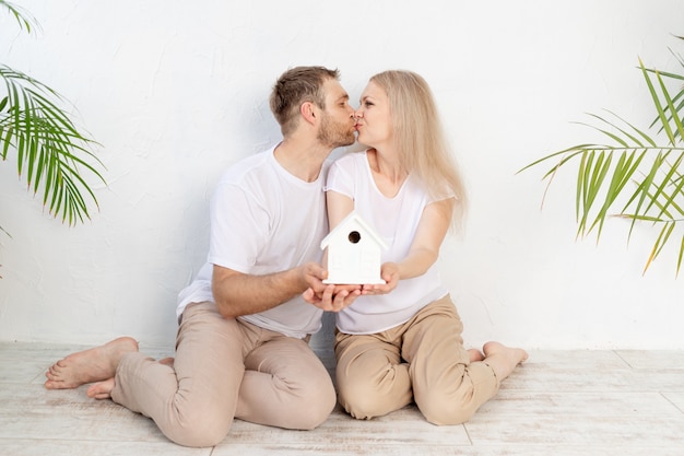 Una pareja feliz, un hombre y una mujer, sostienen una maqueta de una casa en sus brazos y se besan, el concepto de vivienda o una hipoteca para una familia joven