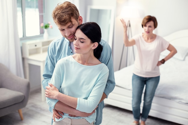 Pareja feliz. hombre positivo alegre de pie detrás de su esposa mientras la abraza