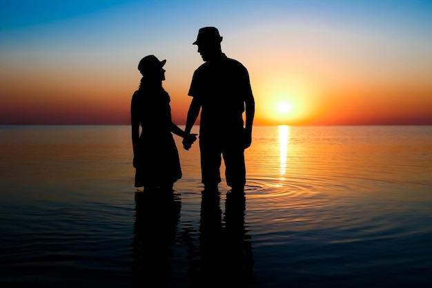 Una pareja feliz junto al mar al atardecer en silueta de viaje en la naturaleza