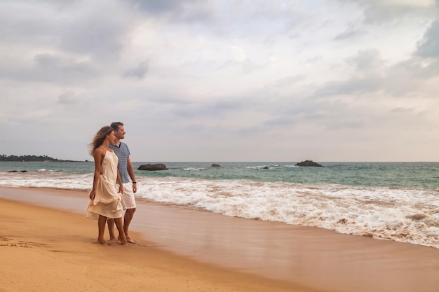 Pareja feliz juntos abrazándose en la playa de arena tropical en el fondo del mar Pareja de belleza disfrutando del verano de luna de miel en la costa del océano