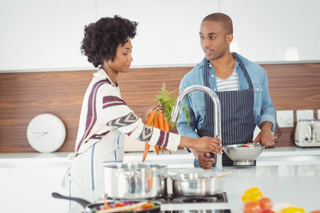 Pareja feliz lavando verduras en la cocina