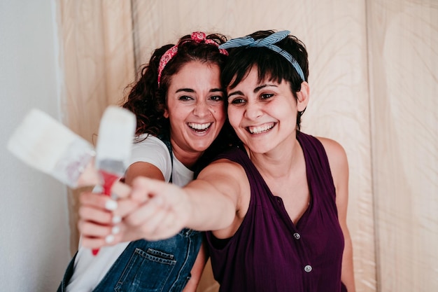 Foto pareja feliz de lesbianas pintando las paredes de la habitación con color blanco hazlo tú mismo y nuevo concepto de casa