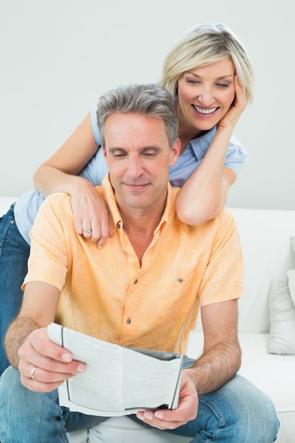 Pareja feliz leyendo el periódico en la sala de estar