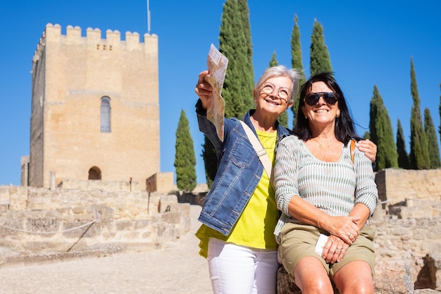 Pareja feliz de mujeres mayores visitando un castillo histórico en Andalucía España descansando mirando el paisaje