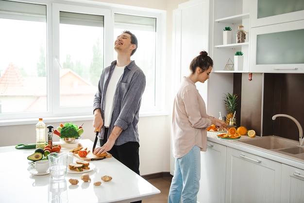 Pareja feliz pasando el fin de semana juntos en la cocina donde preparan un almuerzo saludable vegetariano ...