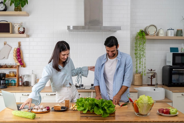 Pareja feliz de pie en la cocina en casa preparando una deliciosa cena parejas casadas hablando disfrutando de una cálida conversación y el proceso de cocinar cuidado de la salud comiendo ensalada de verduras frescas