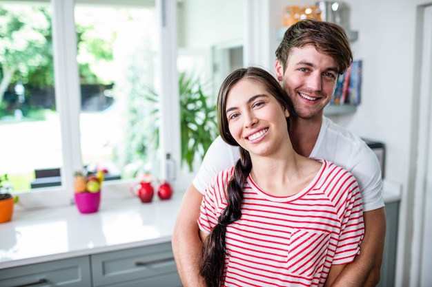 Pareja feliz de pie en la cocina y mirando a la cámara