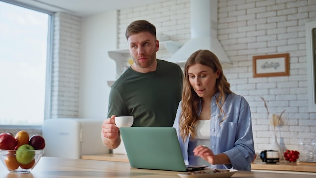 Una pareja feliz planea vacaciones mirando el portátil, la cocina, el primer plano, los cónyuges hablando.