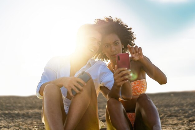 Pareja feliz en la playa con teléfono móvil - jóvenes amantes viendo contenido divertido de las redes sociales de Internet en el teléfono inteligente sentado en la arena