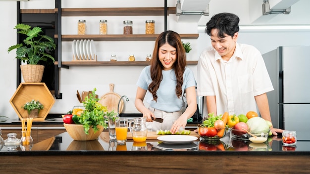 Una pareja feliz prepara y cocina ensalada saludable con verduras en una tabla de cortar juntos.